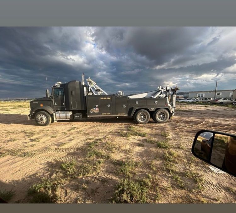 A black tow truck is parked in a dirt field