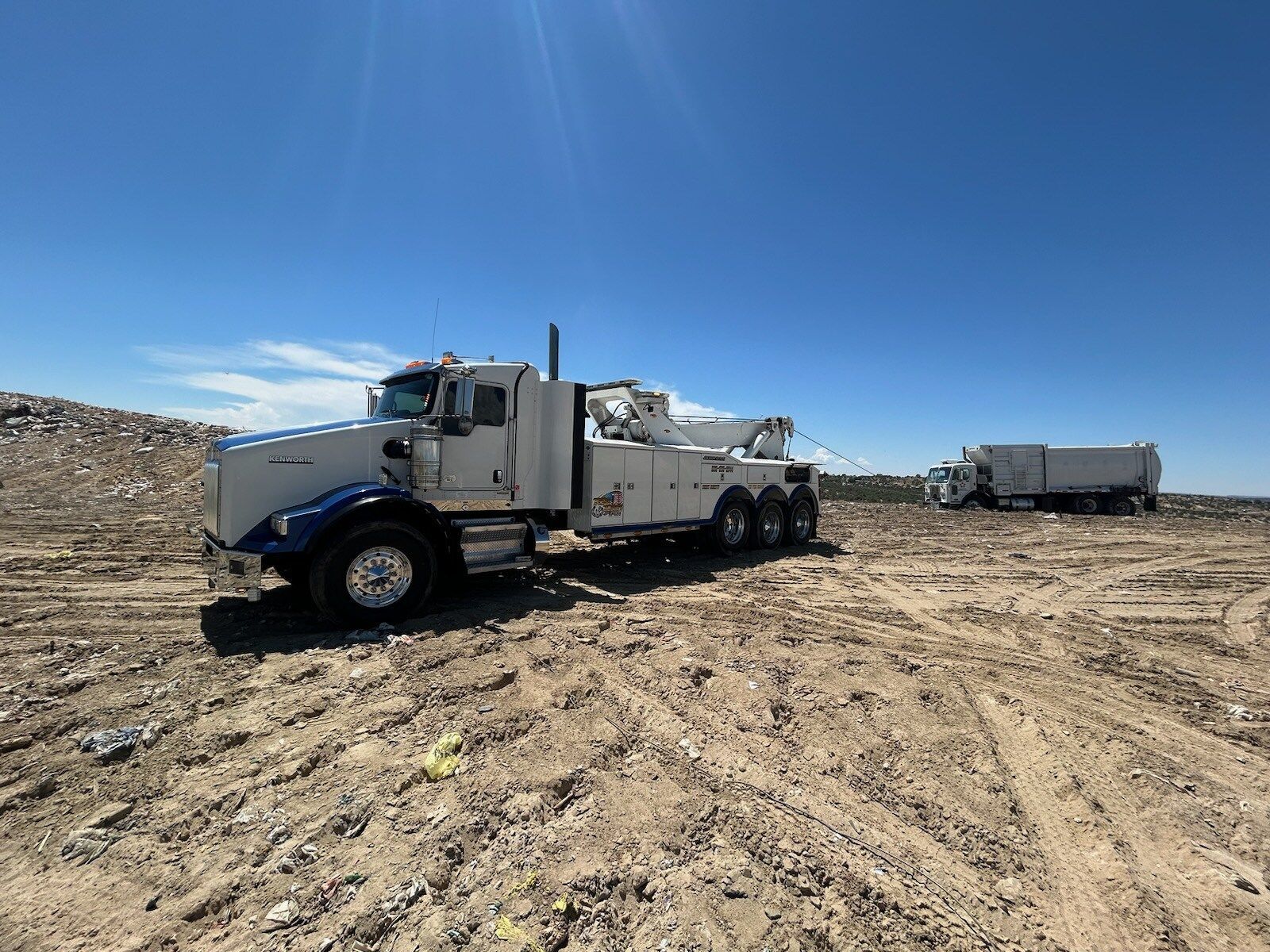 A tow truck is parked in the middle of a dirt field.