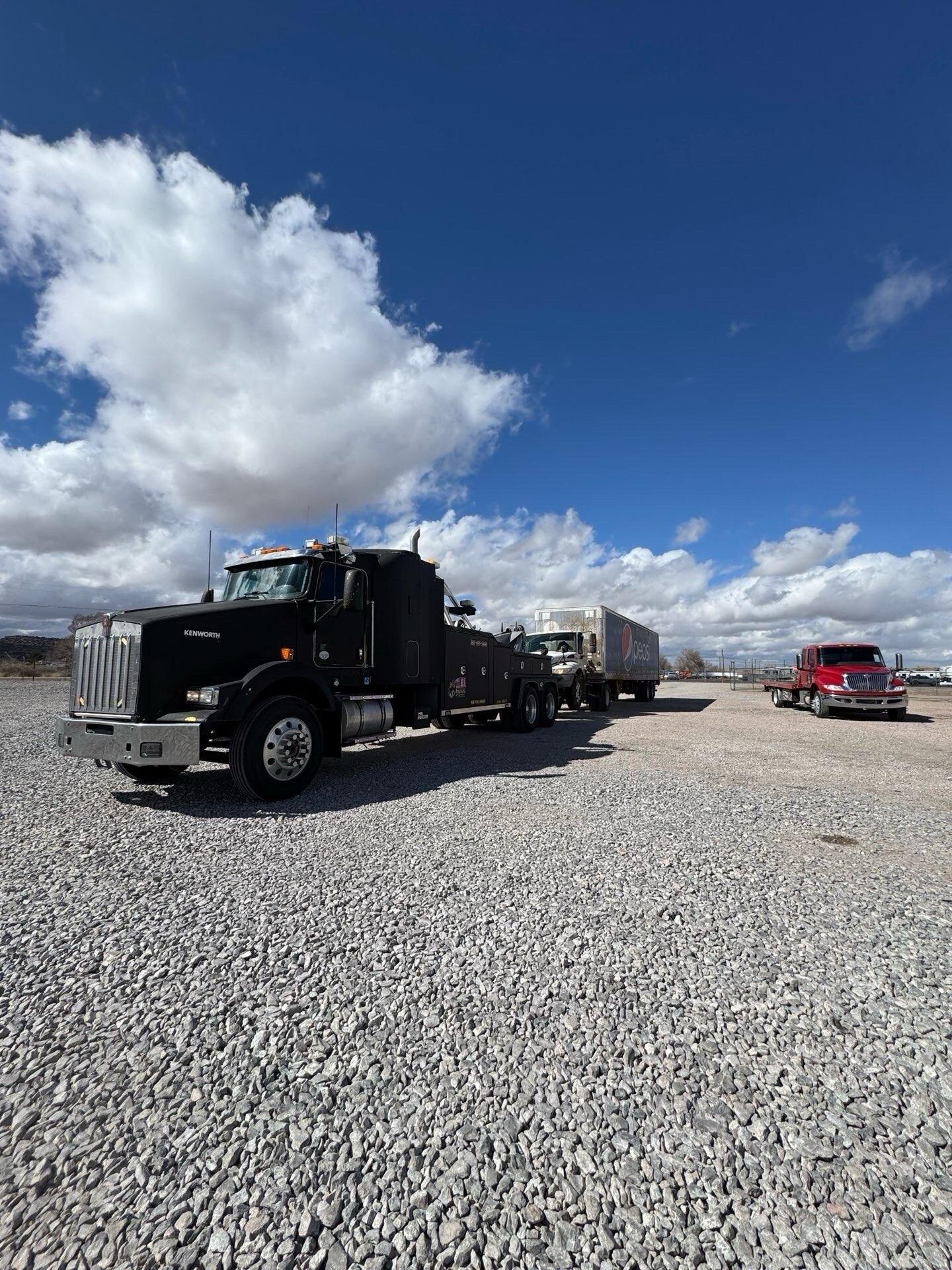 A black semi truck is parked in a gravel lot next to a red truck.