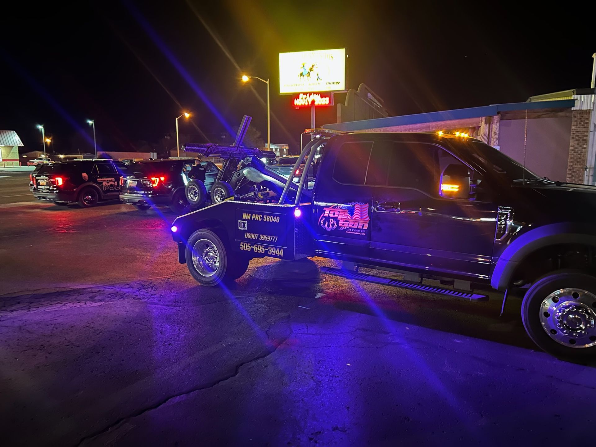 A tow truck is towing a car in a parking lot at night.