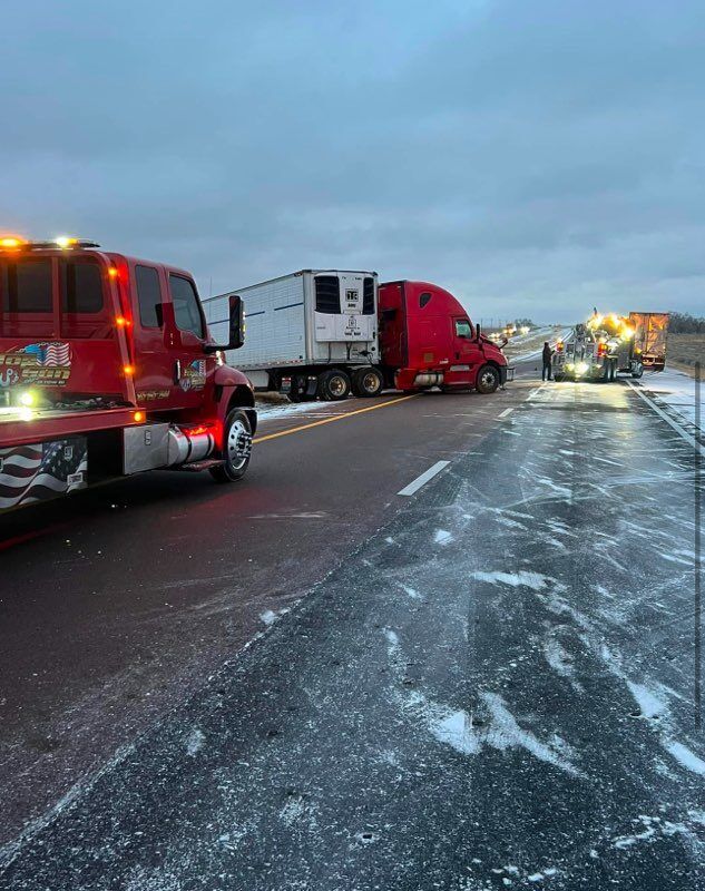 A red tow truck is towing a semi truck on a snowy highway.