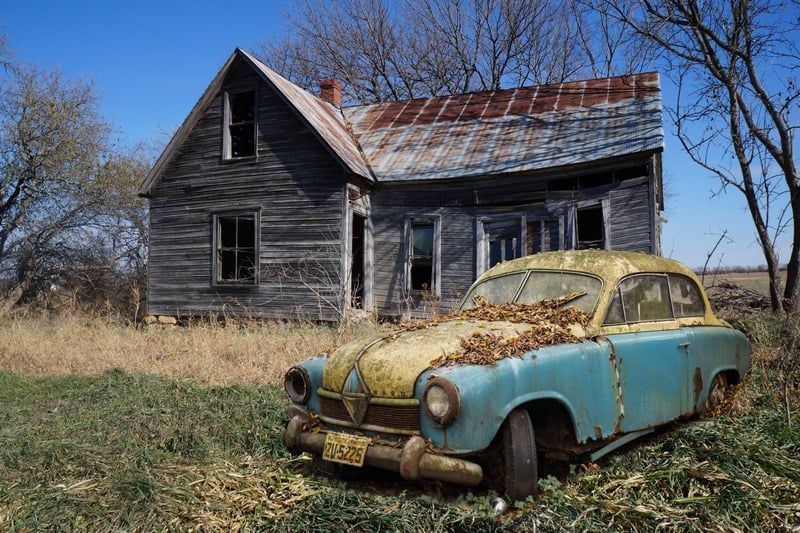 An old car is parked in front of an abandoned house.