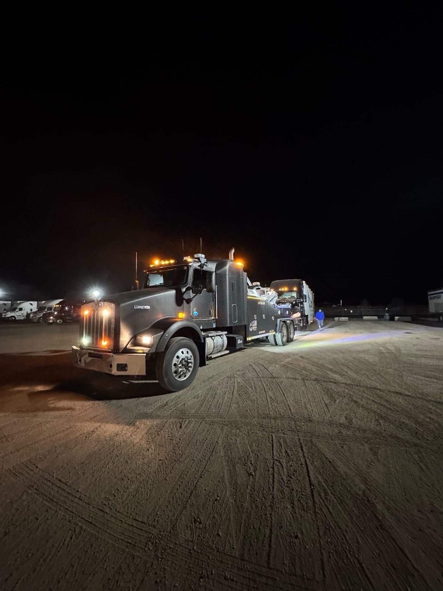 A large semi truck is parked in a dirt lot at night.