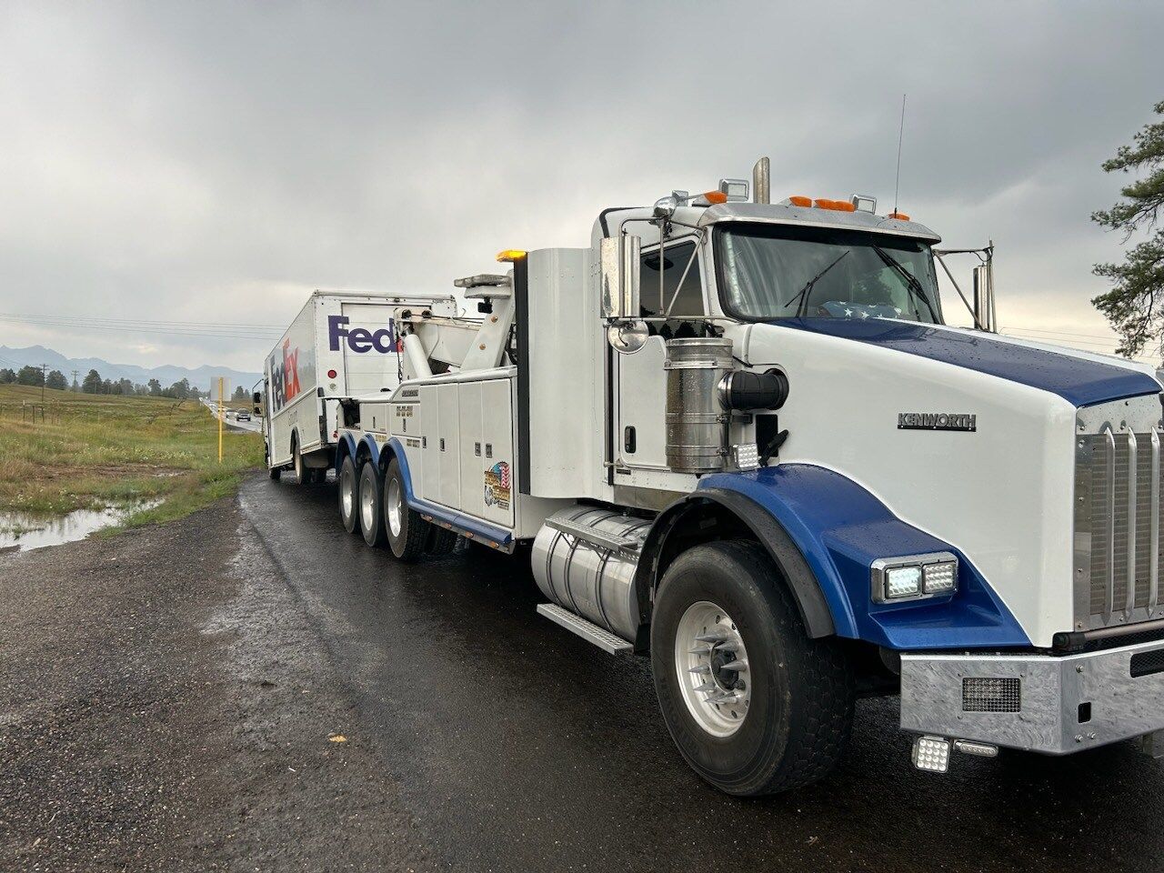 A white and blue tow truck is parked on the side of the road.