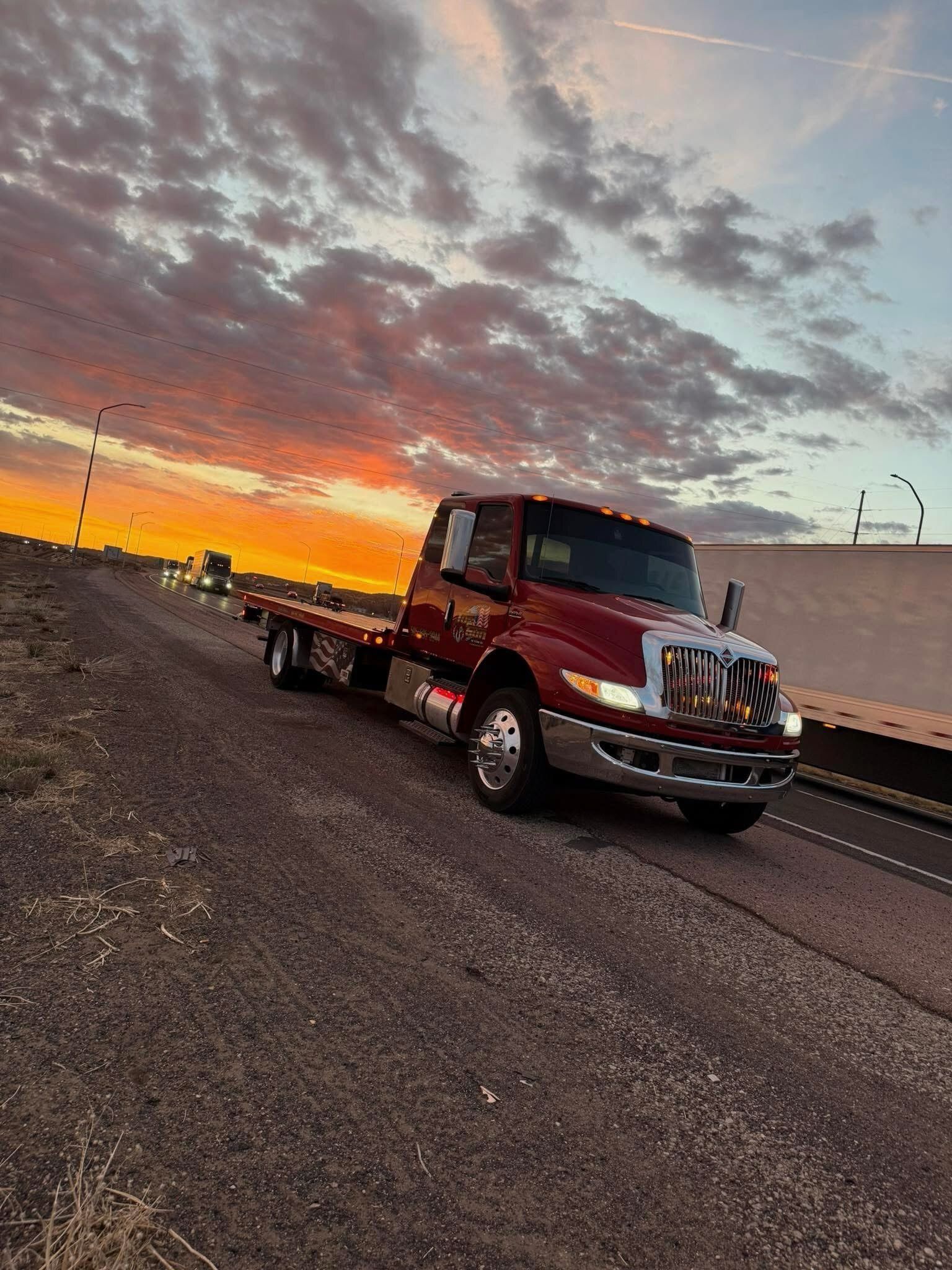 A red tow truck is driving down a road at sunset.