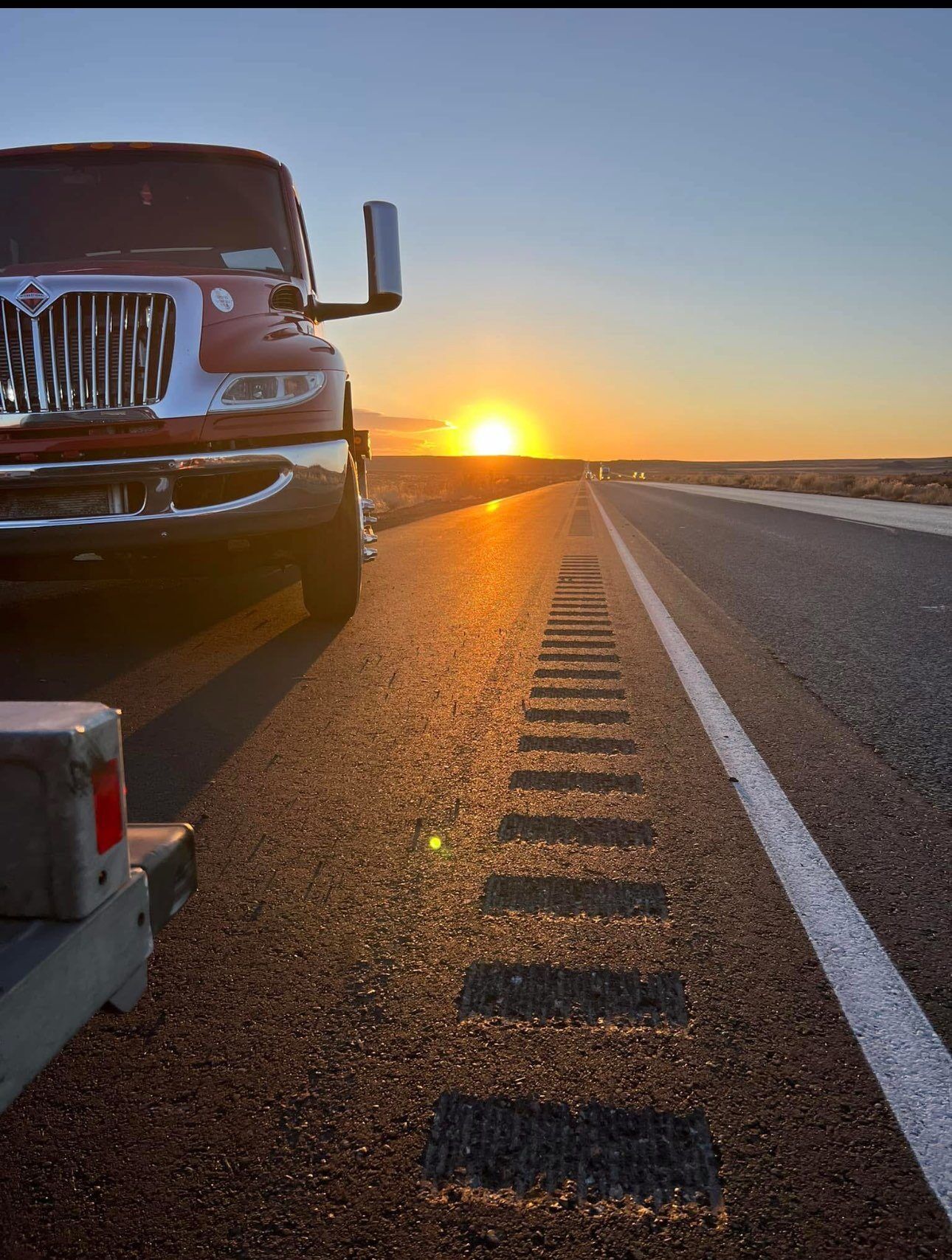 A truck is parked on the side of a highway at sunset.