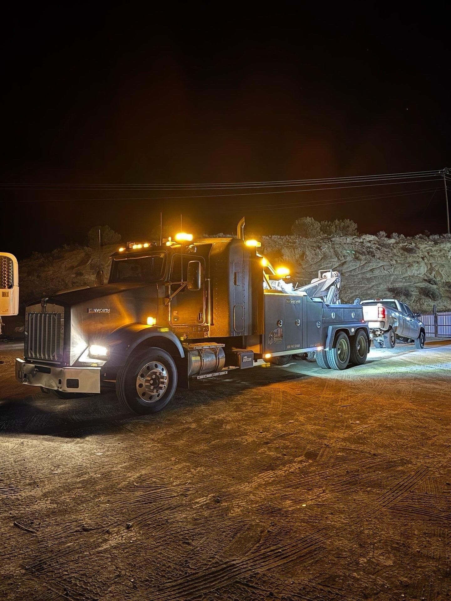 A tow truck is parked in a gravel lot at night.