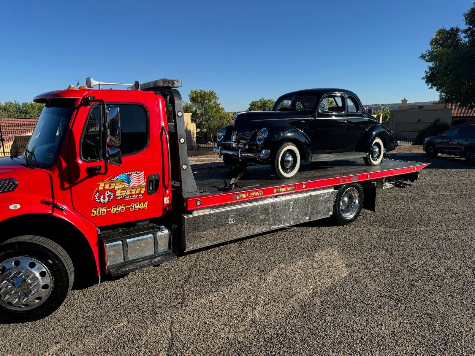 A red tow truck is carrying a black car on the back of it.