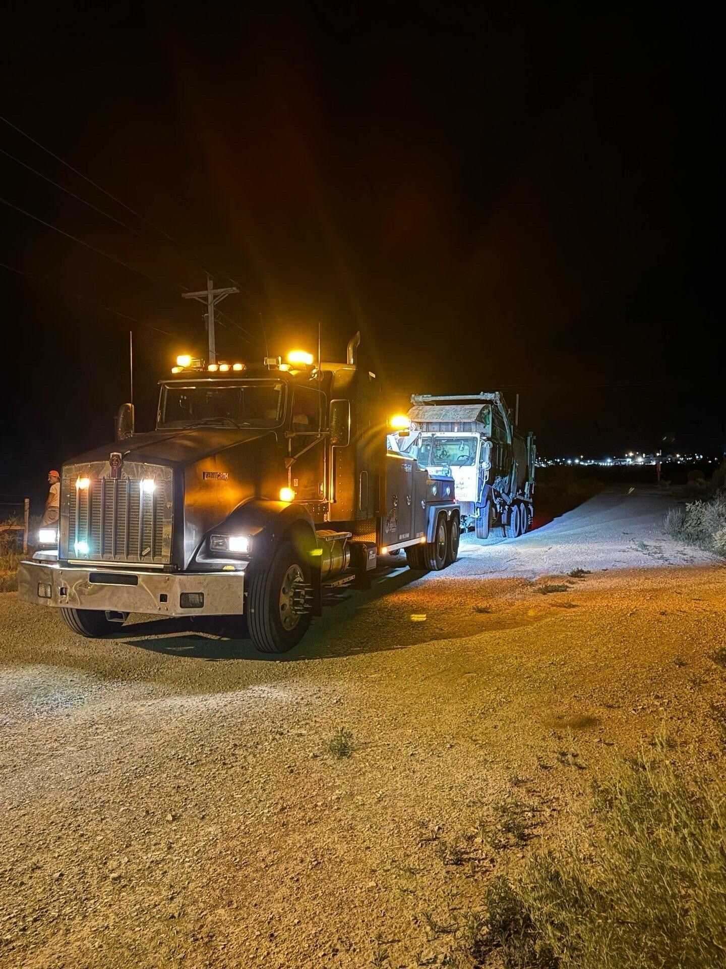 A semi truck is driving down a gravel road at night.