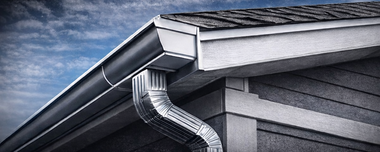 Gutter system on a house with gray siding and roof against a blue sky.
