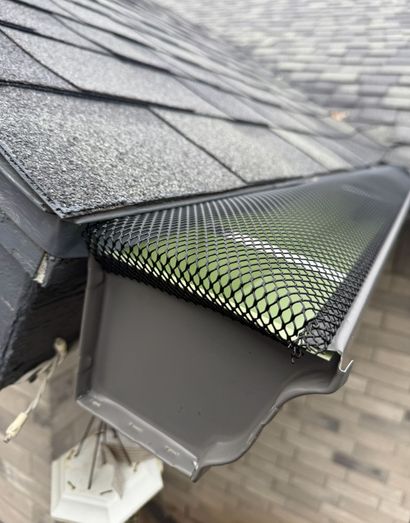 Gray roof gutter with black mesh guard installed.