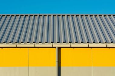 Gray corrugated metal roof over a yellow and beige building with a blue sky background.