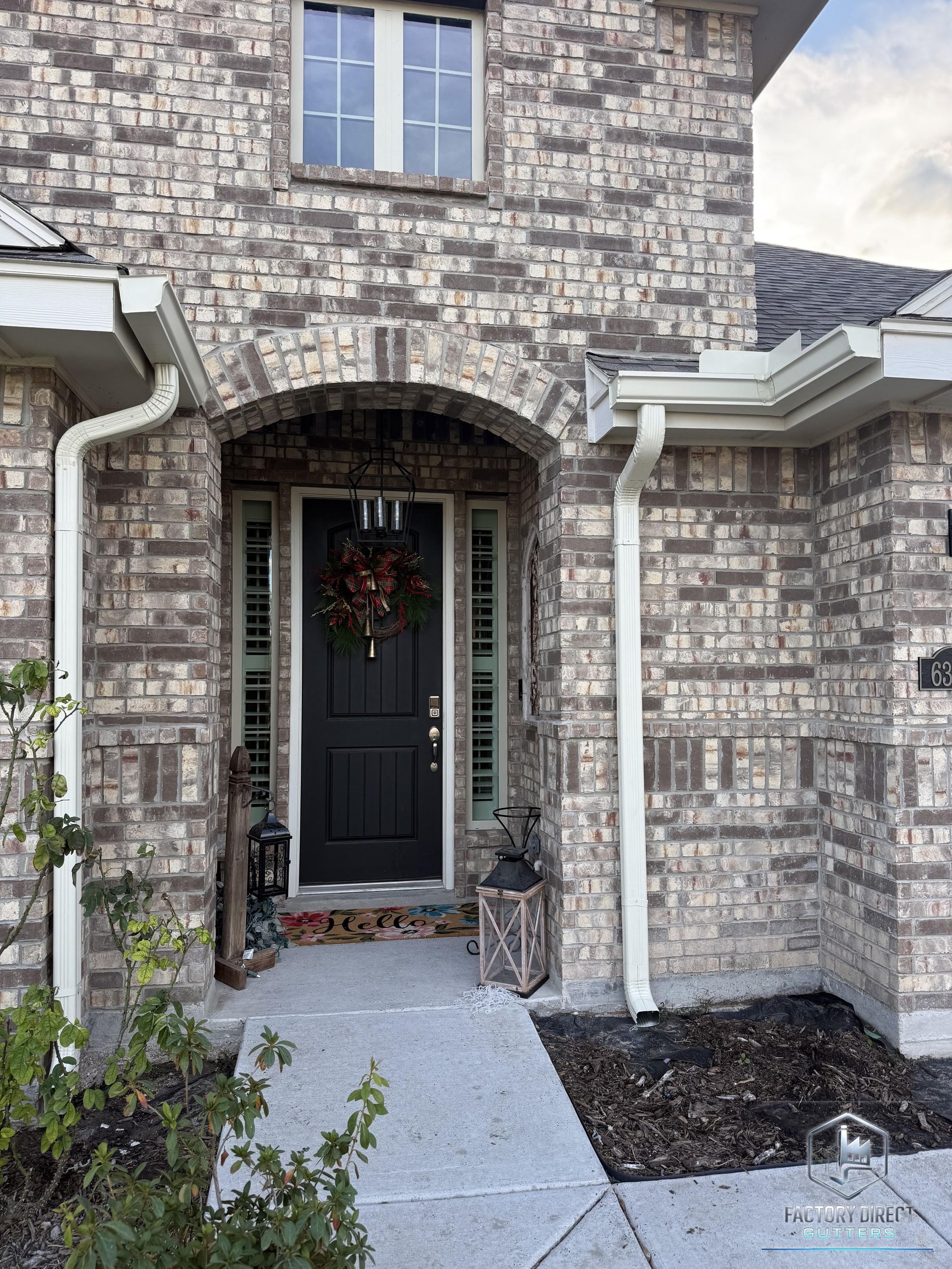 Brick house entrance with black door, arched doorway, and white gutters.