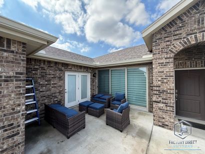 Patio with brick walls, blue cushions on wicker furniture, French doors, and a blue sky.