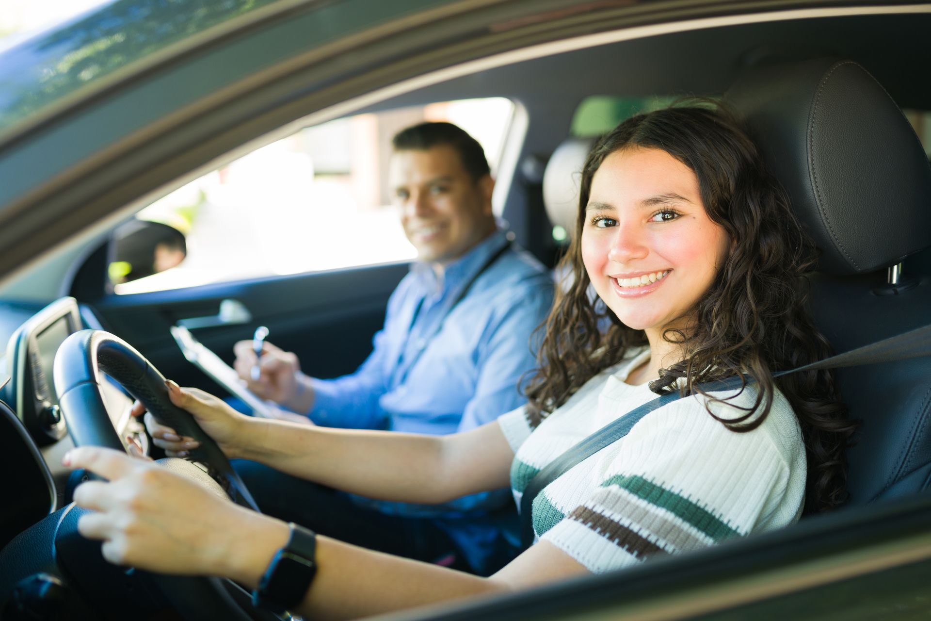 Teen driving lesson with instructor taking notes in the passenger seat.