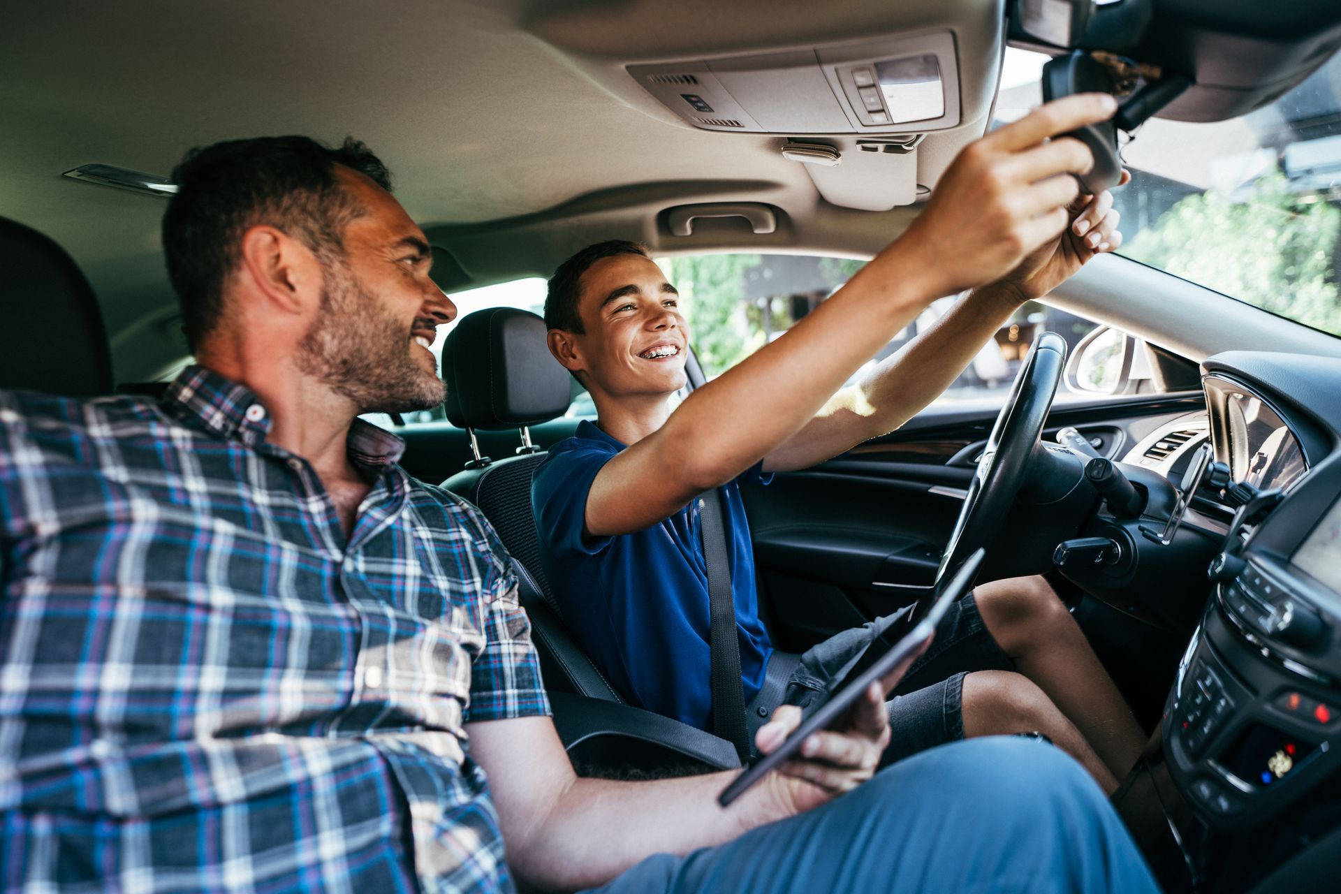 A driving instructor and his student in a car cabin explaining how to prepare the safety mirror. A driving instructor and his student in a car cabin explaining how to prepare the safety mirror.