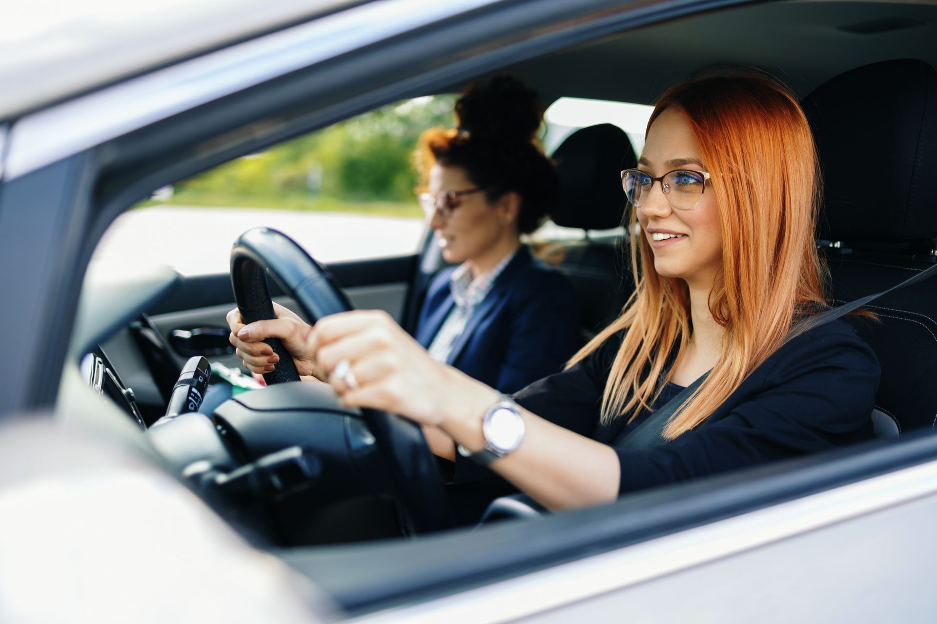 Two women are sitting in a car looking at their phones.