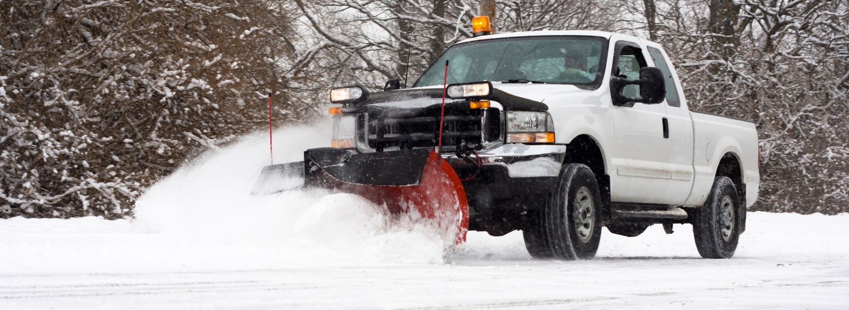 A white truck is plowing snow on a snowy road.