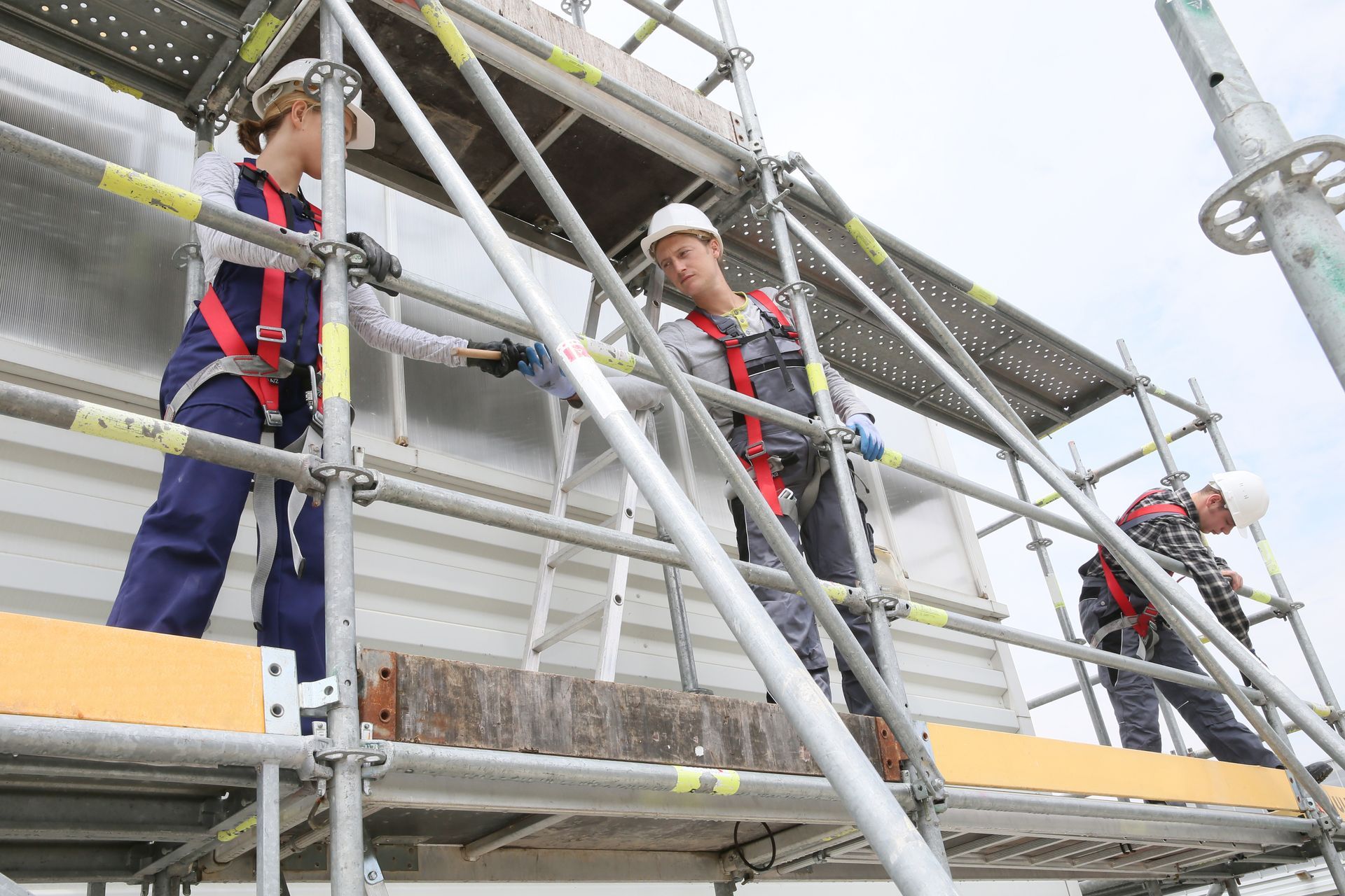 A group of builders wearing protective gear is installing scaffolding on site.