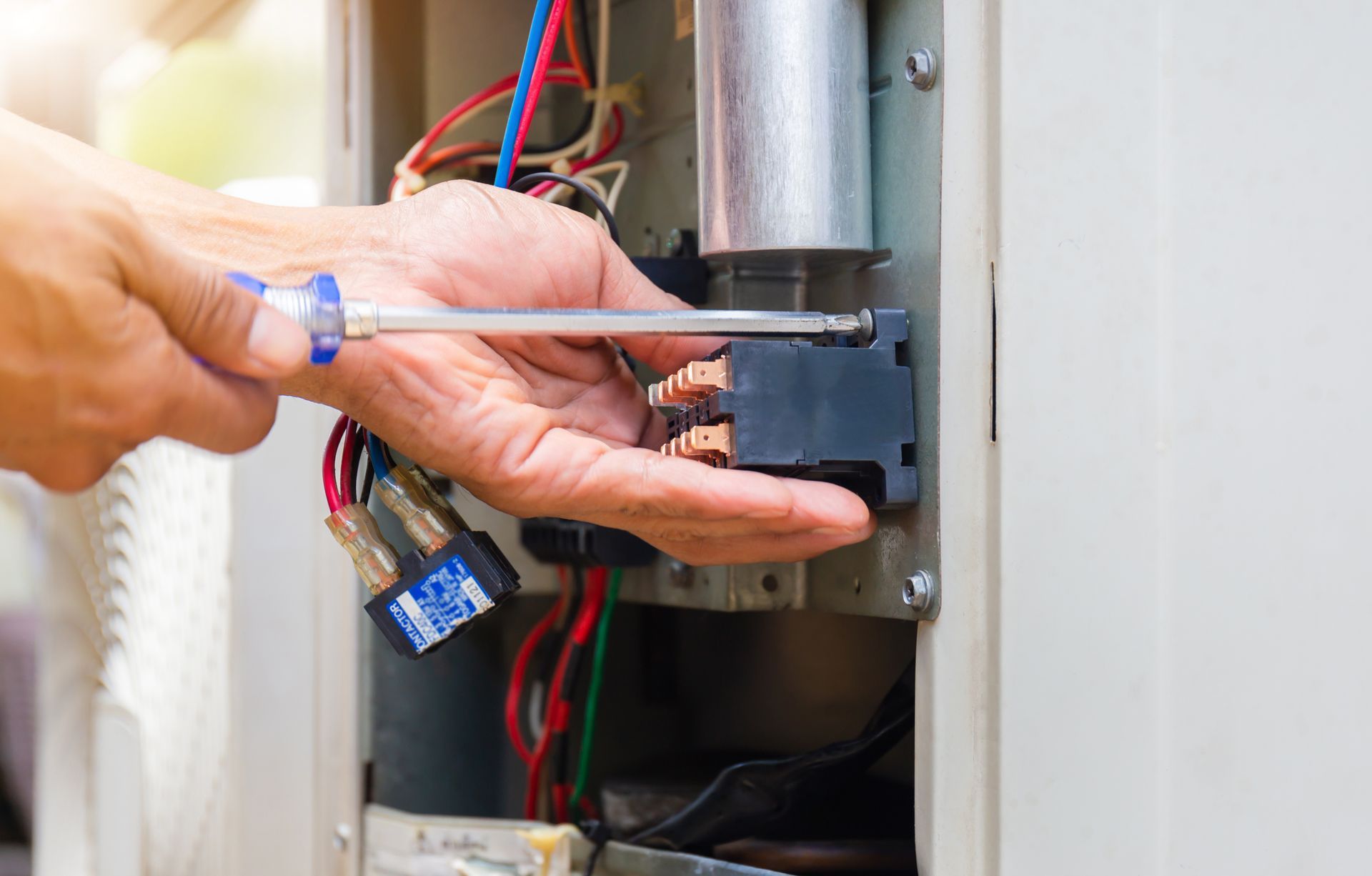 A furnace repair technician fixing electrical components inside a heating unit.