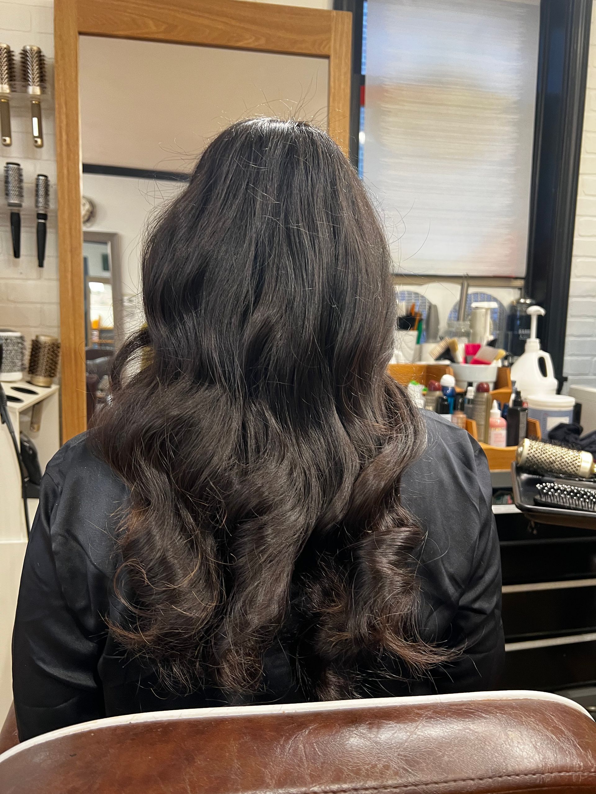 A woman with long hair is sitting in a chair in front of a mirror.