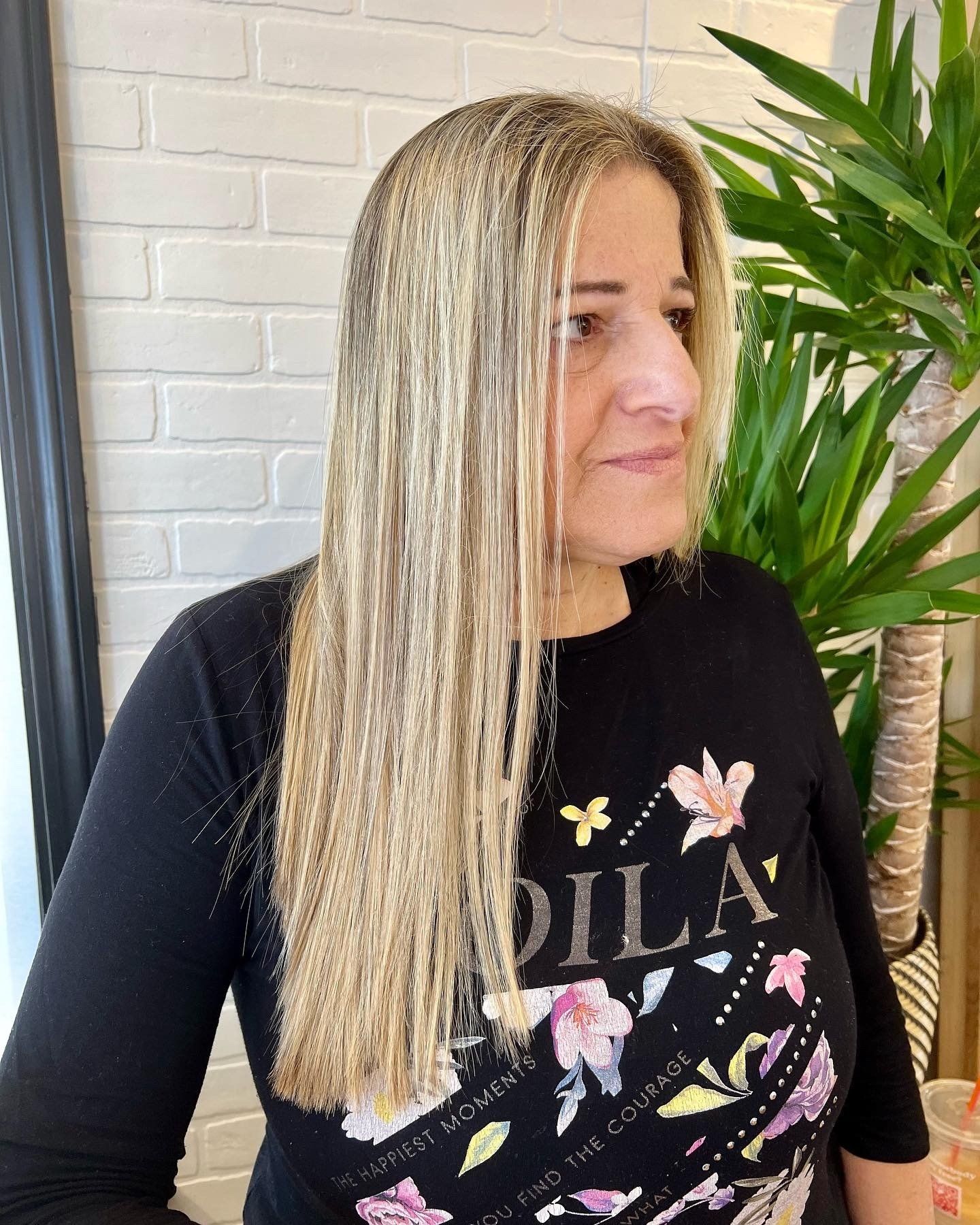 A woman with long blonde hair is wearing a black shirt with flowers on it.