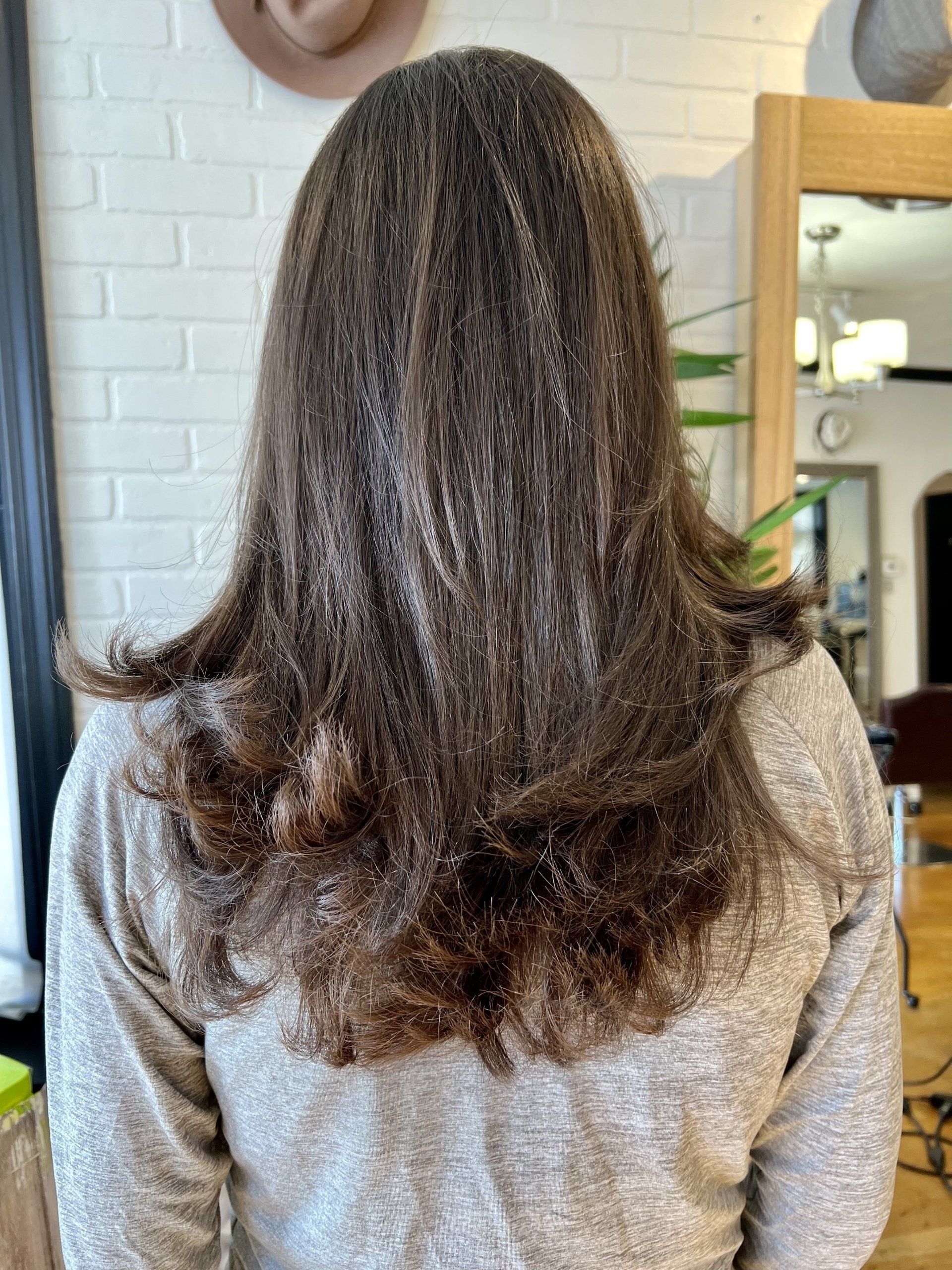 A woman with long hair is standing in front of a mirror in a salon.