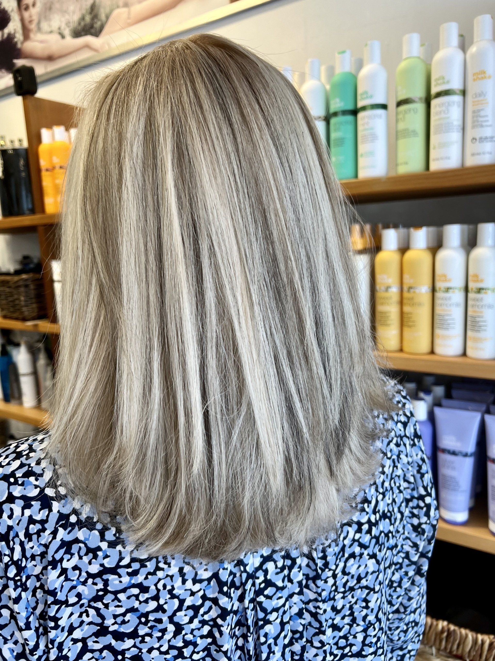 A woman with blonde hair is sitting in front of a shelf of hair products.