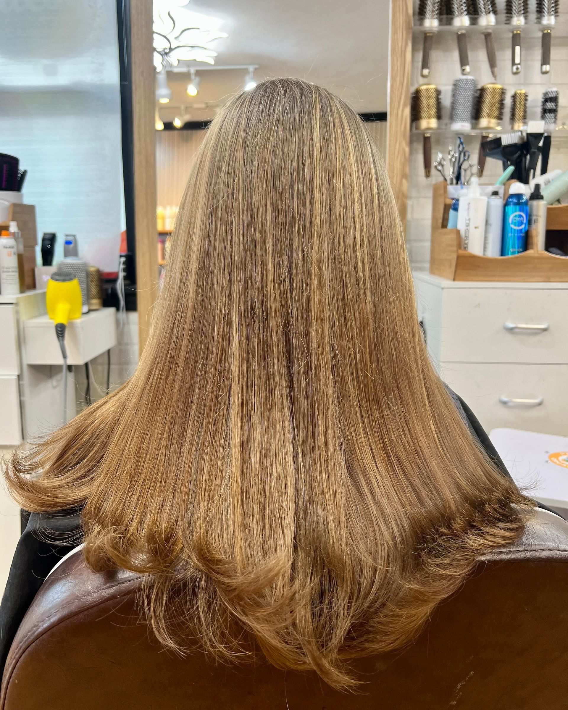 A woman with long blonde hair is sitting in a chair in a salon.