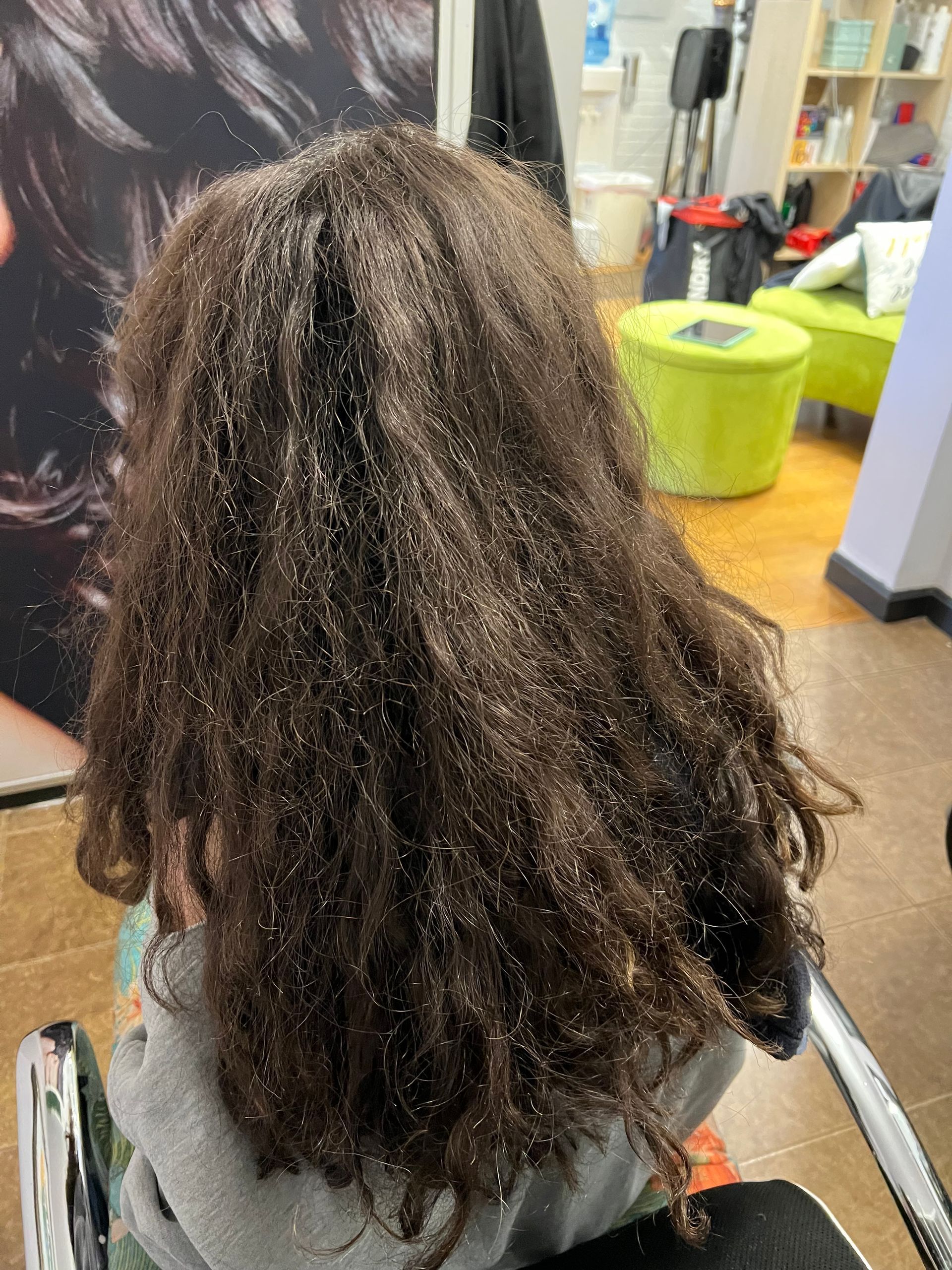 A little girl with long hair is sitting in a chair in a salon.