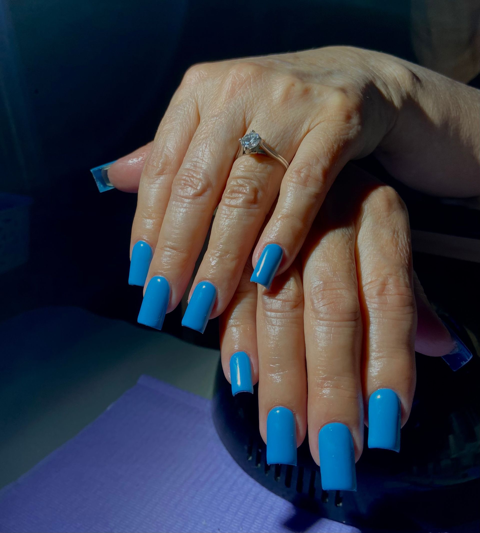 A woman 's hands with blue nails and a ring on her finger.