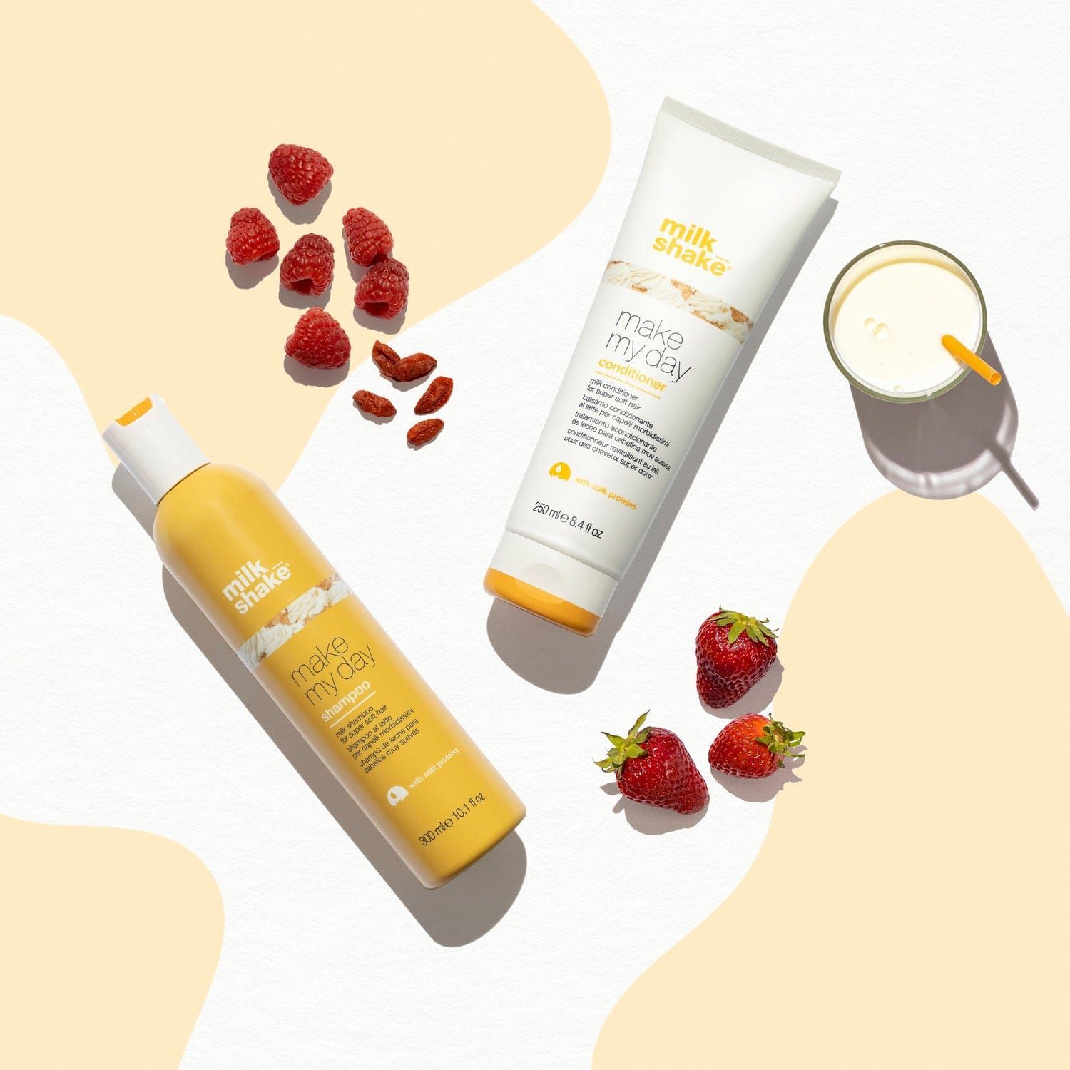 A bottle of milkshake shampoo and conditioner next to strawberries and a glass of milk.