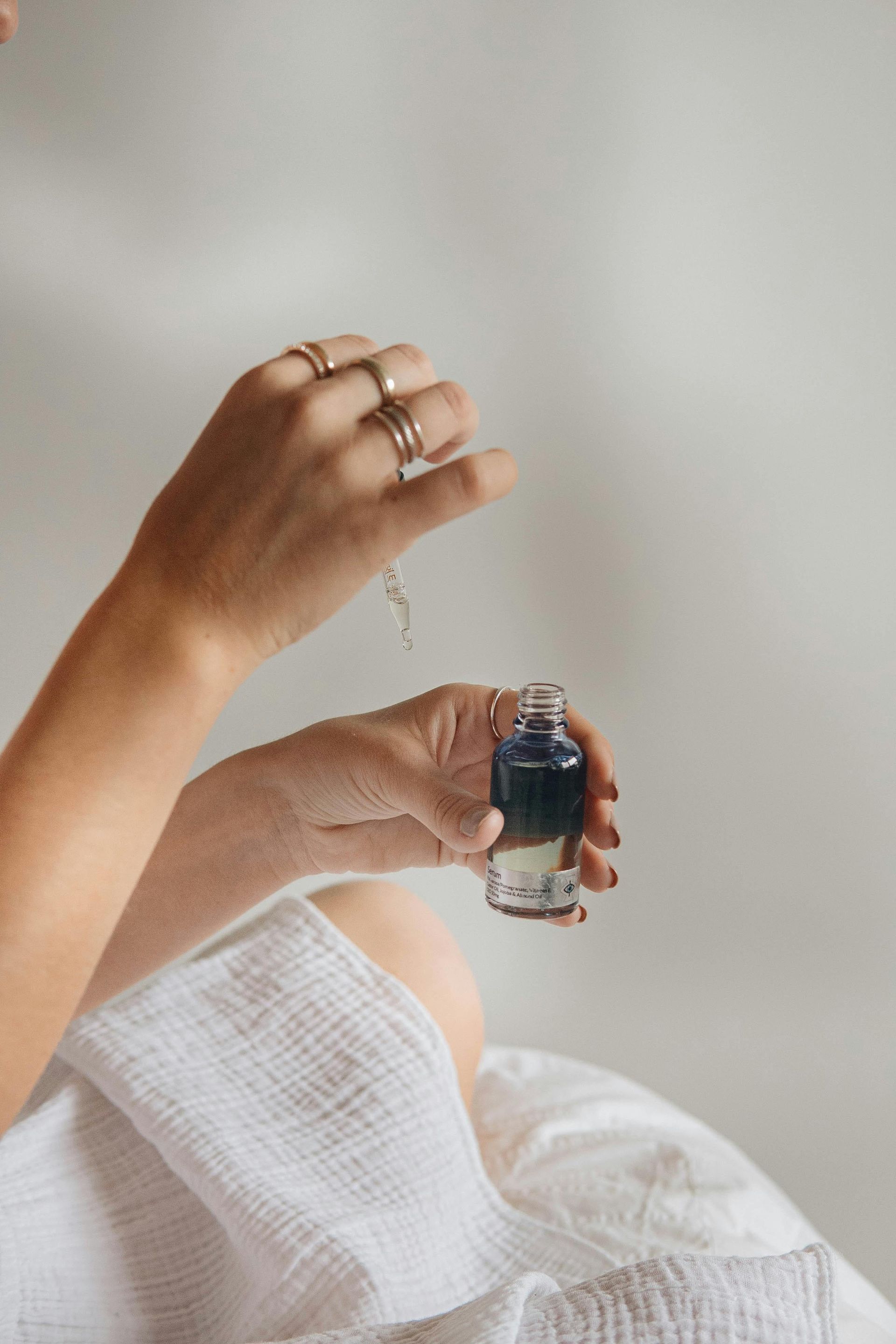 Person holding a small dark bottle and dropper, adding drops to the skin. Rings on fingers in walpole ma