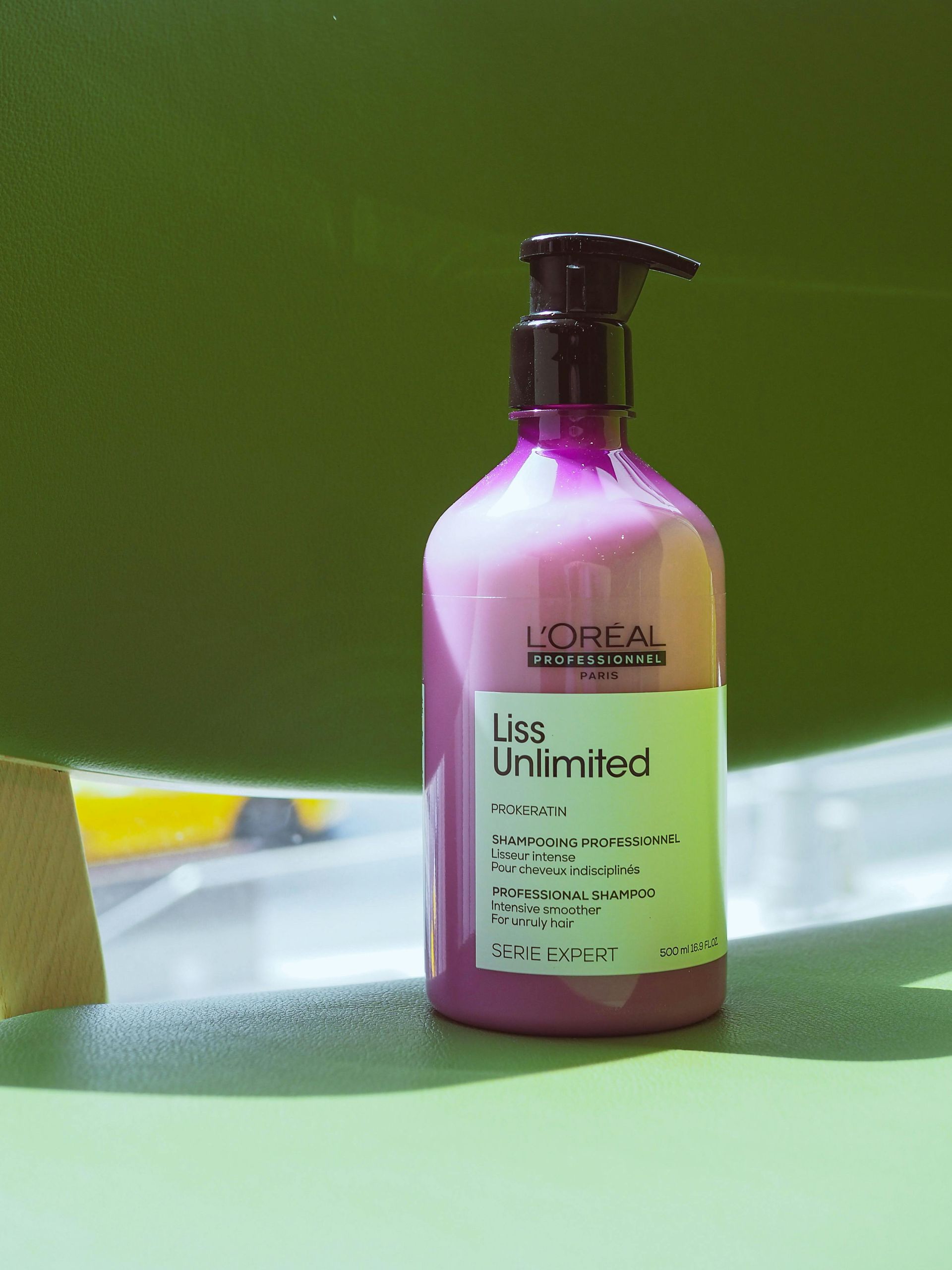 Pink L'Oreal Liss Unlimited hair product bottle with a black pump against a green background in newton ma