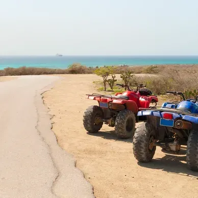 Two atvs are parked on the side of a road next to the ocean.
