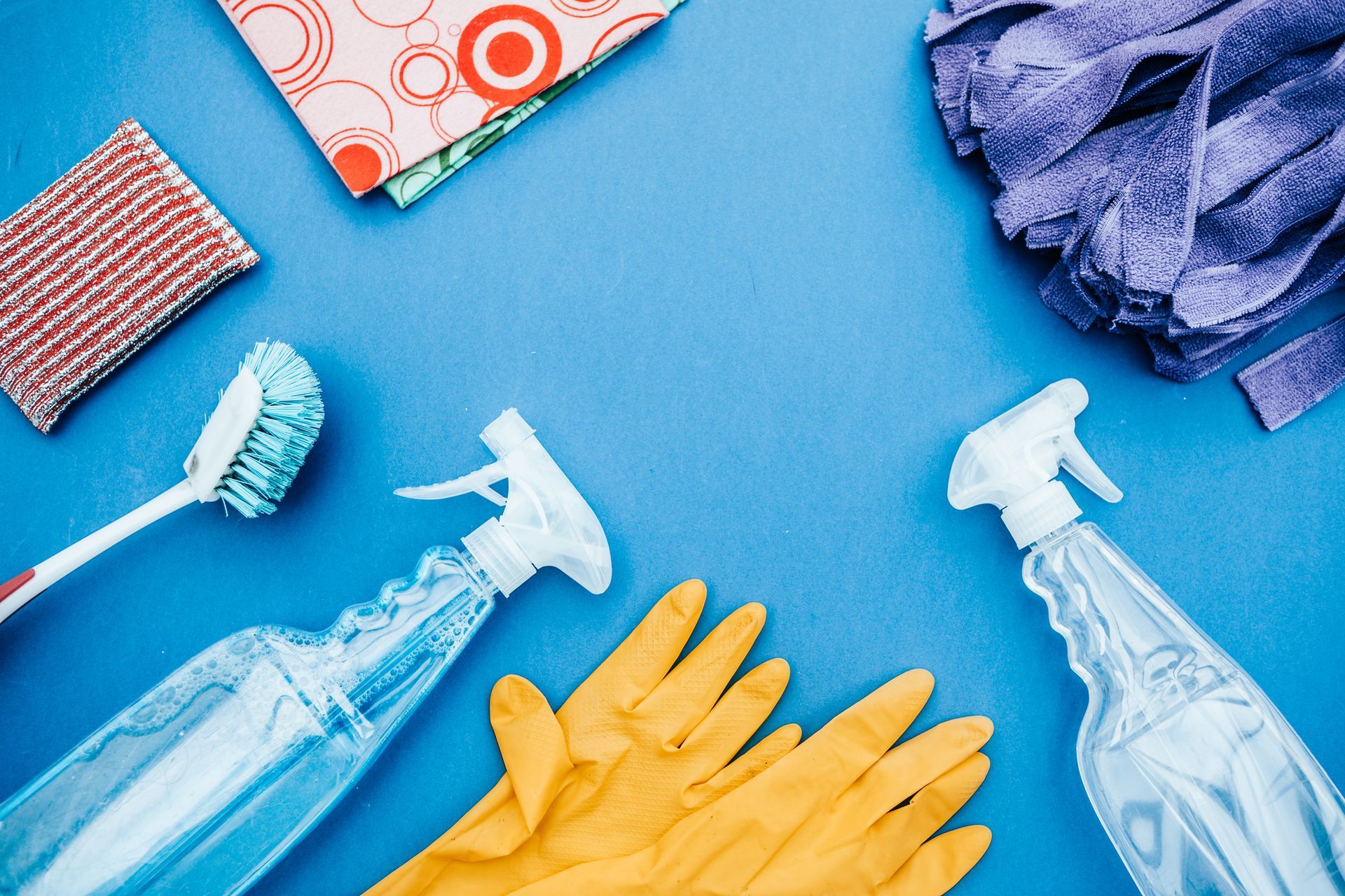 Prodotti per la pulizia in blu: flaconi spray, guanti, spazzola, spugne e panni in microfibra.