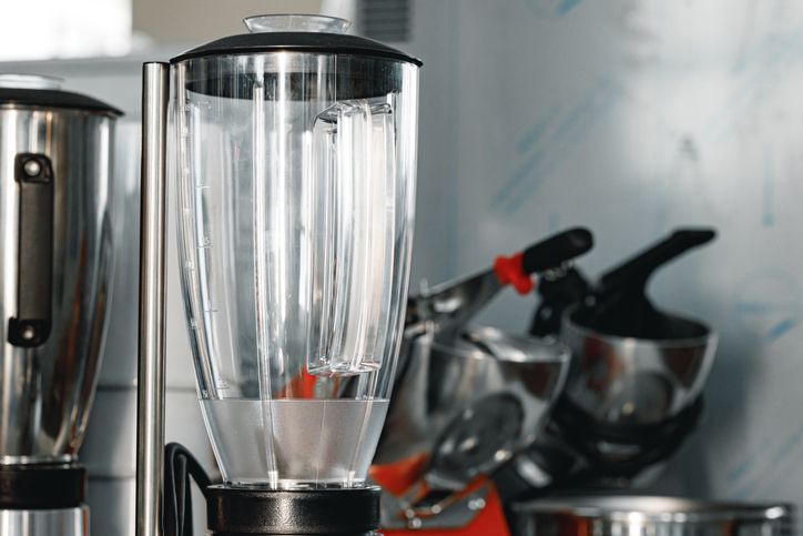 Frullatore con contenitore trasparente in un ambiente da cucina; sono visibili altri elettrodomestici in acciaio inossidabile.