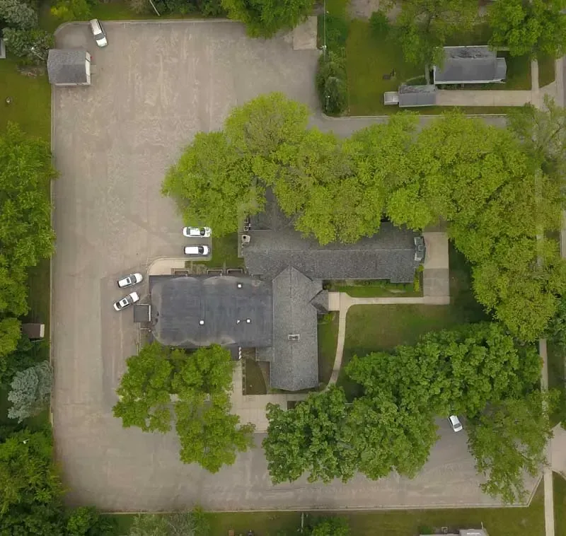 An aerial view of a house surrounded by trees and a parking lot.