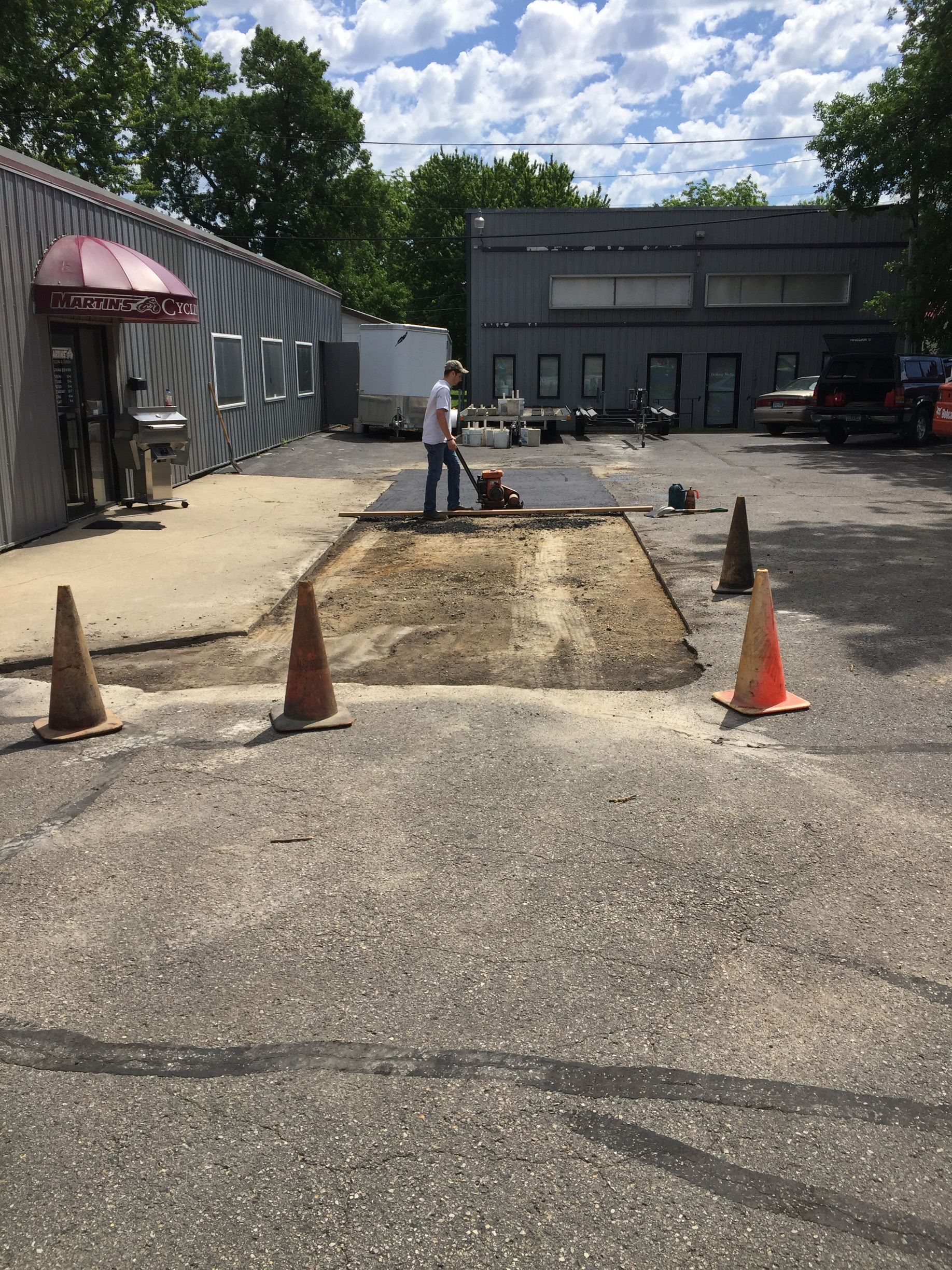 A man is laying asphalt in a parking lot next to a building.