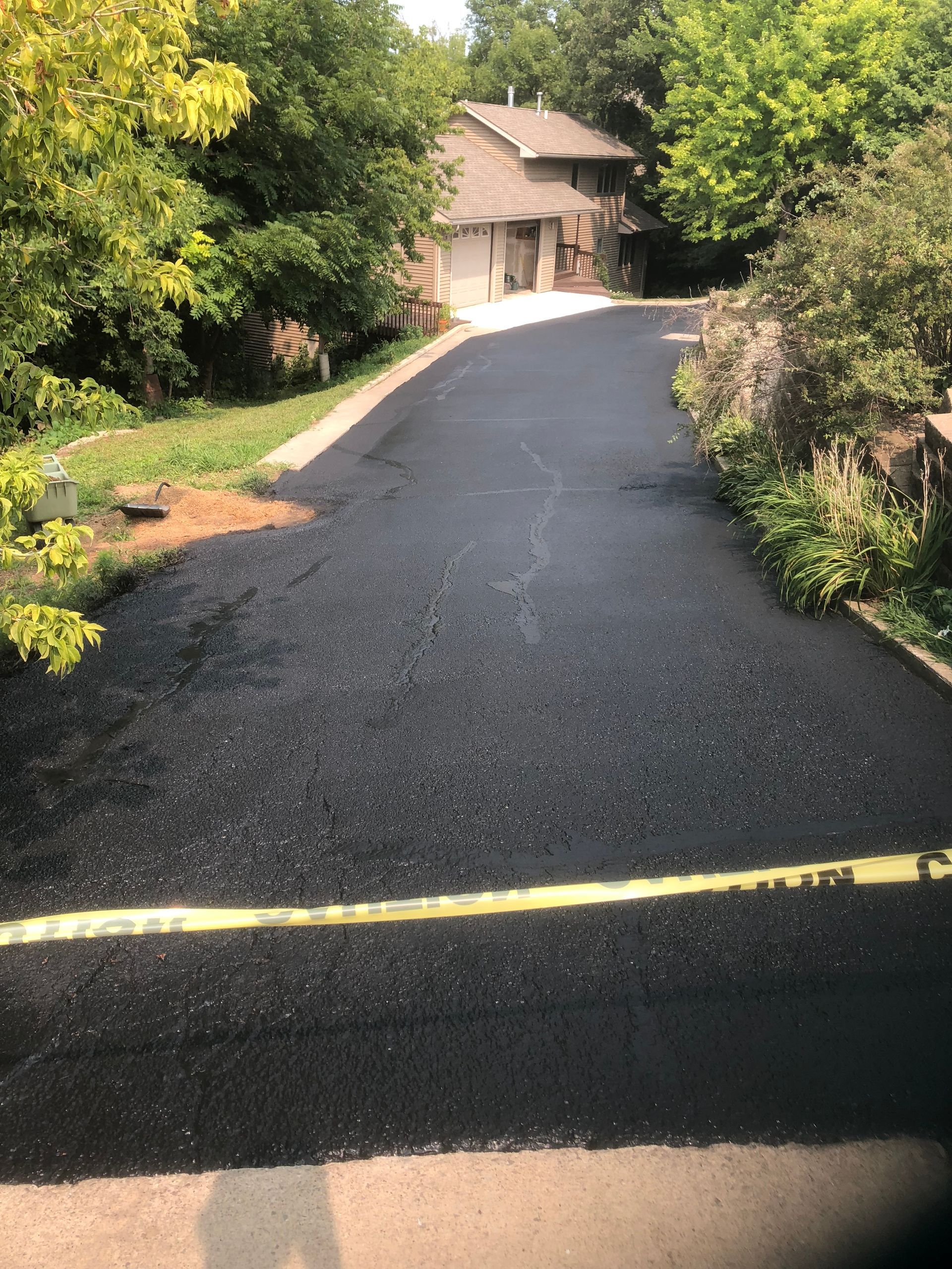 A black asphalt driveway leading to a house surrounded by trees.