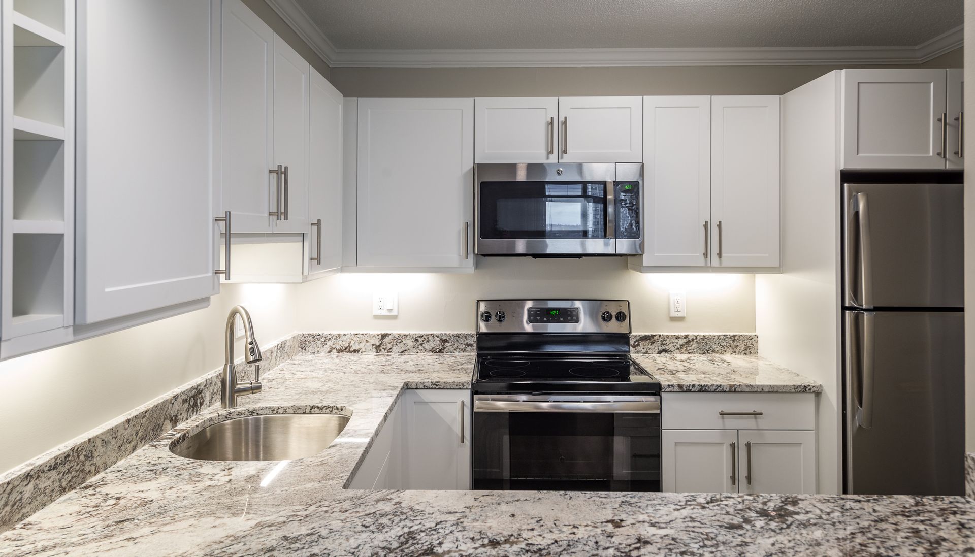 Modern white kitchen with granite countertops and stainless steel appliances.