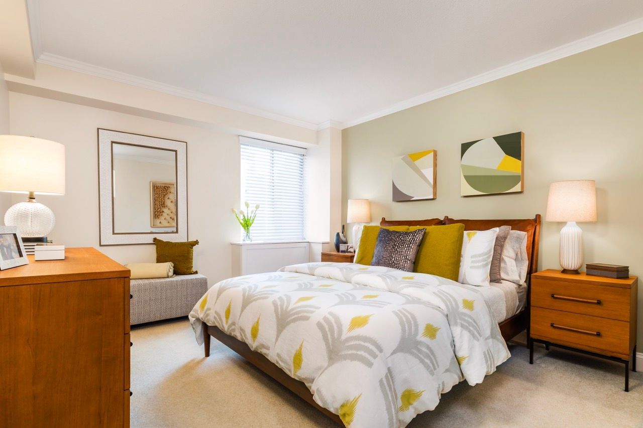 Bedroom with a wooden bed, two nightstands, lamps, window with blinds, and abstract wall art.