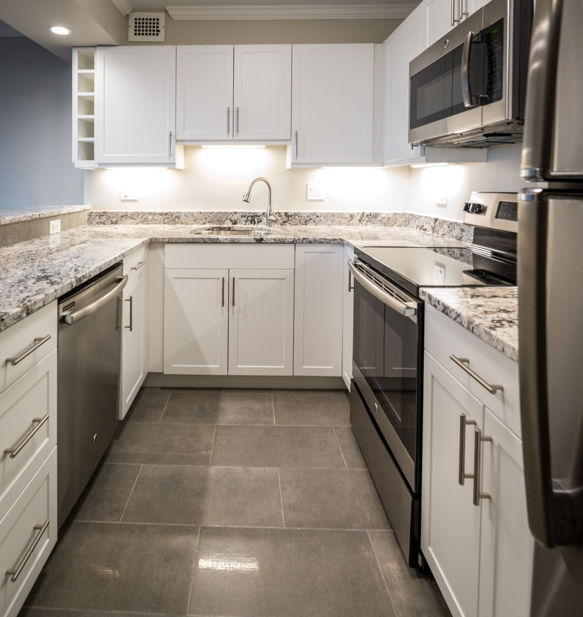 Modern L-shaped kitchen with white cabinets, granite countertops, and stainless-steel appliances.