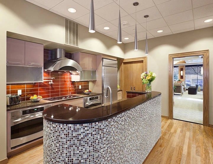 Modern kitchen with curved mosaic island, stainless steel appliances, and pendant lights.