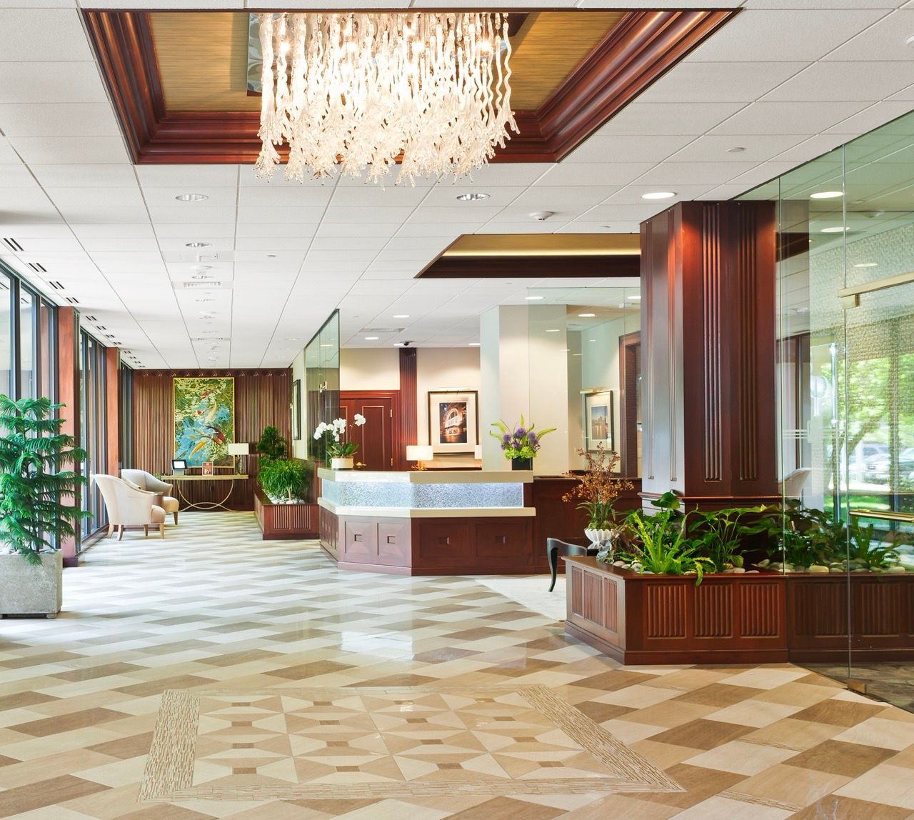 Residential lobby with chandelier, wood paneling, glass walls, and potted plants