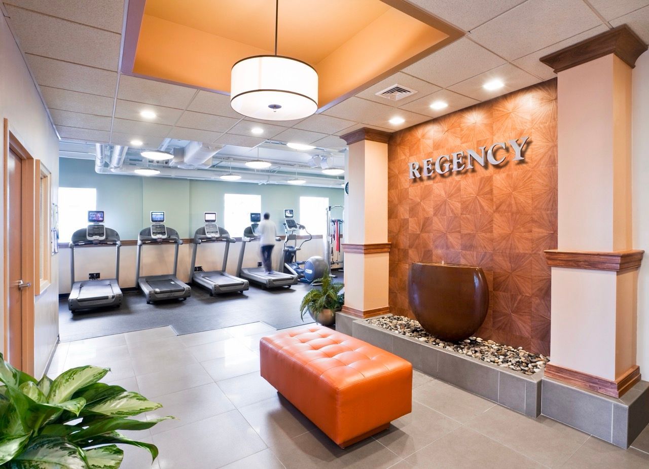 Fitness center with a row of treadmills, a decorative wall, and an orange ottoman.