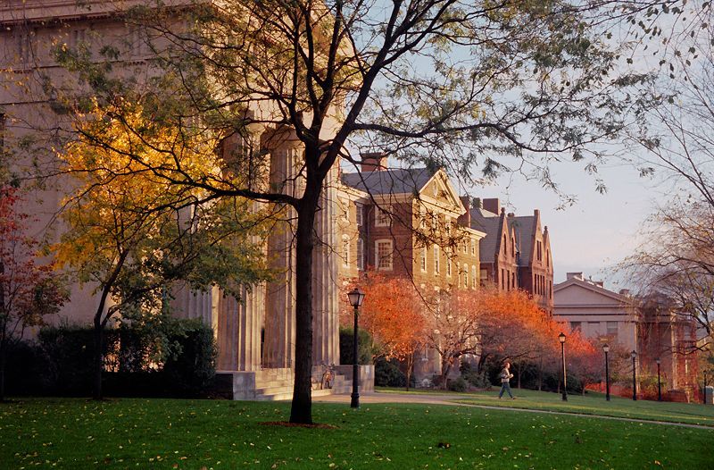 Autumn campus scene with trees, green lawn, and historic brick buildings at sunset