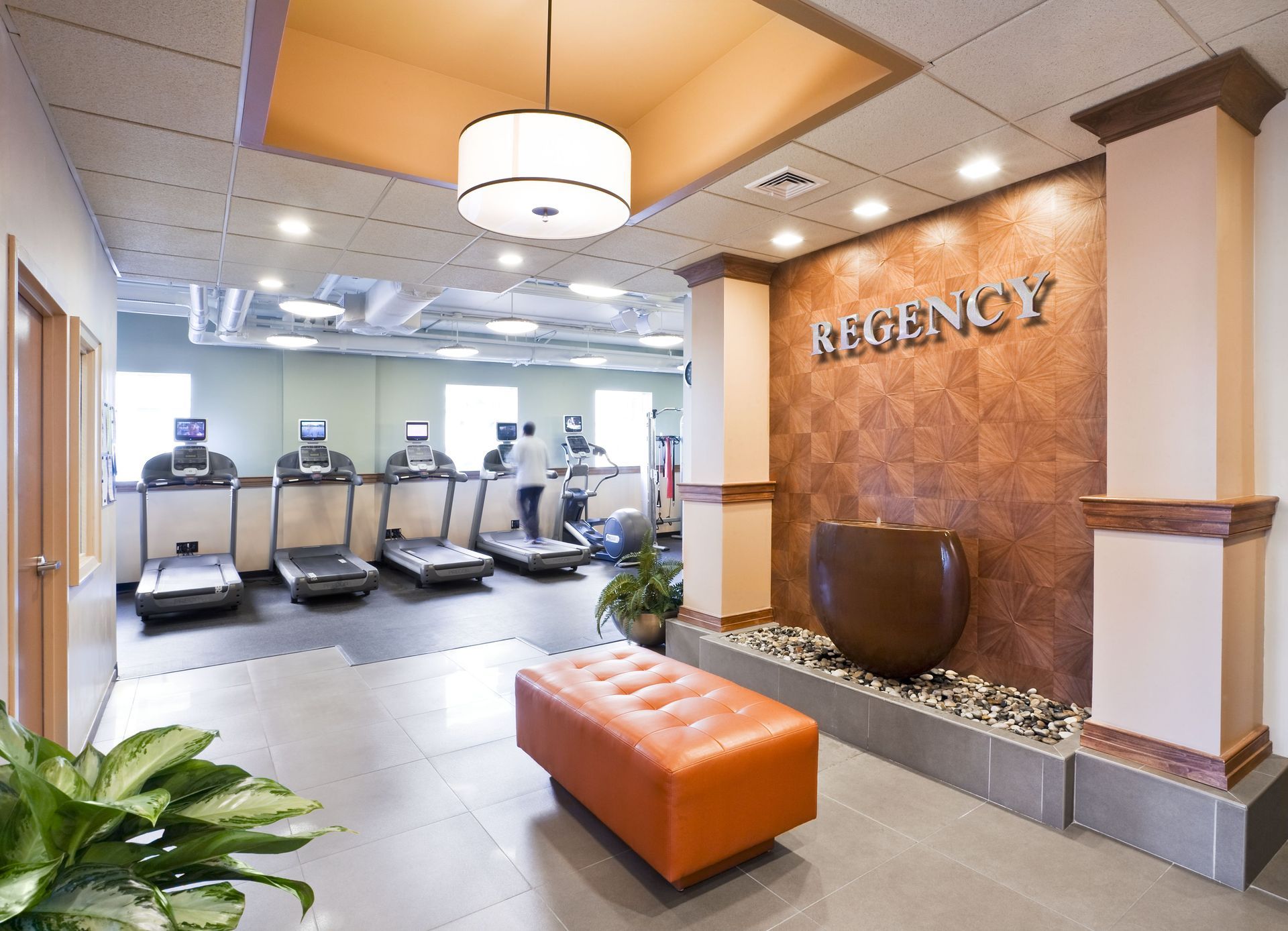Fitness center with a row of treadmills, a decorative wall, and an orange ottoman.