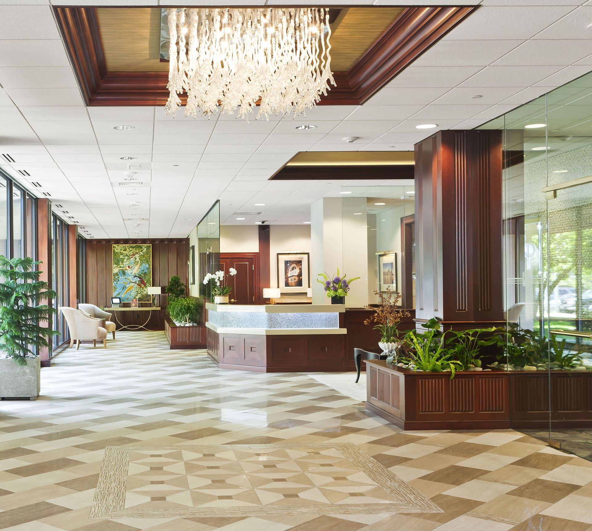 Residential lobby with chandelier, wood paneling, glass walls, and potted plants