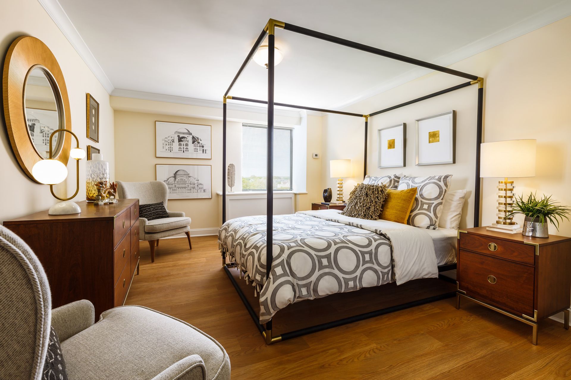 Elegant bedroom with brass canopy bed, patterned bedding, wood furniture, and warm natural light.